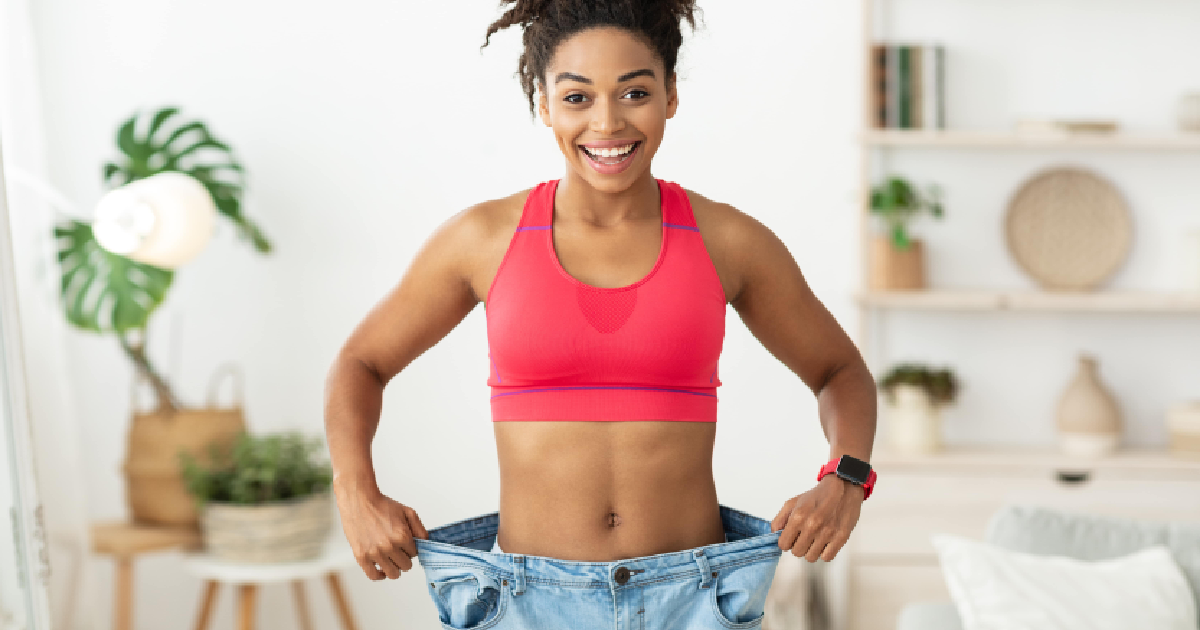 Smiling woman showing weight loss by holding out loose jeans, representing results of Emsculpt Body Contouring in Bonita Springs, FL.